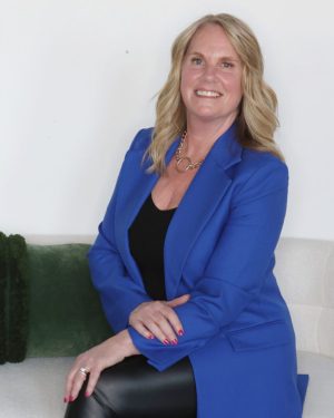 Woman in blue blazer sitting on a white couch, smiling. Woman in blue blazer sitting on a white couch, smiling.